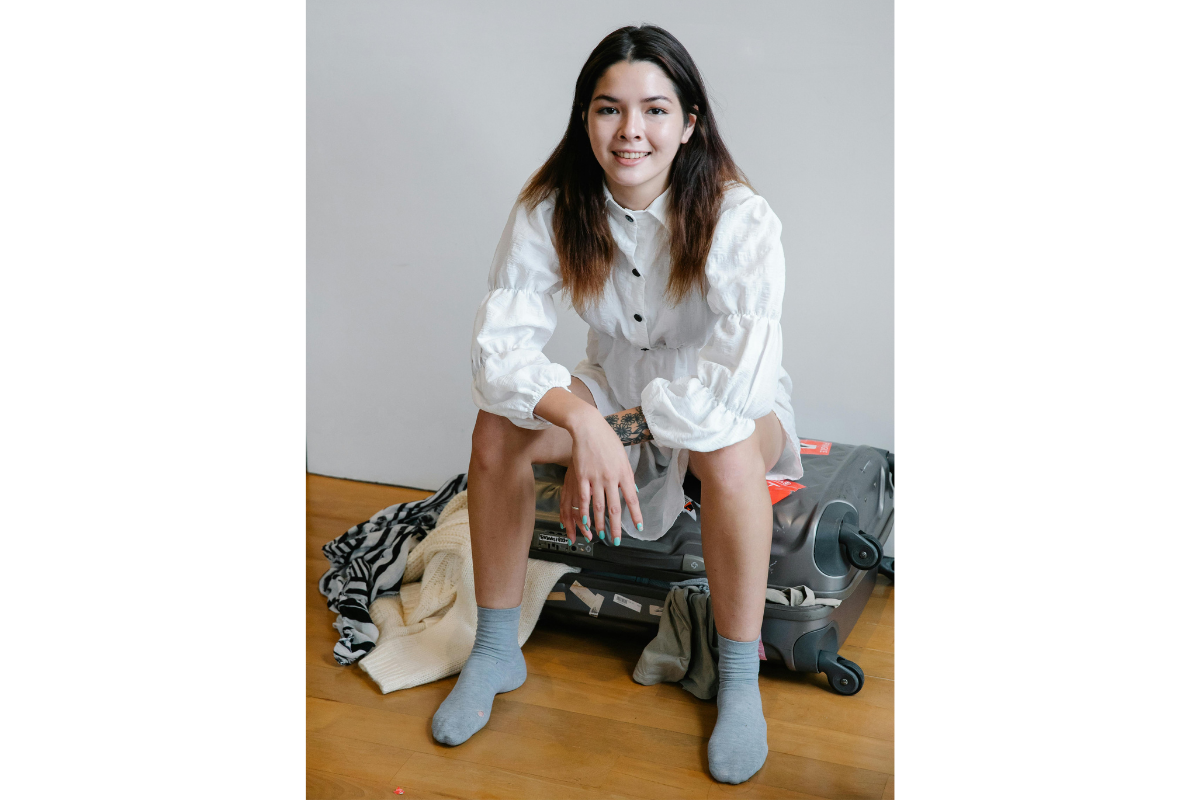 Woman confidently sits on top of overflowing suitcase.